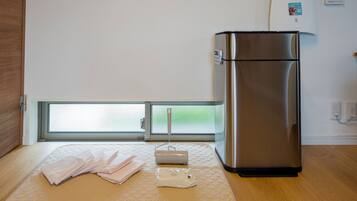 A modern kitchen with a stainless steel refrigerator, a wooden floor, and a window with a view of greenery.
