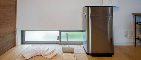 Una cocina moderna con un refrigerador de acero inoxidable, piso de madera y una ventana con vistas a zonas verdes.