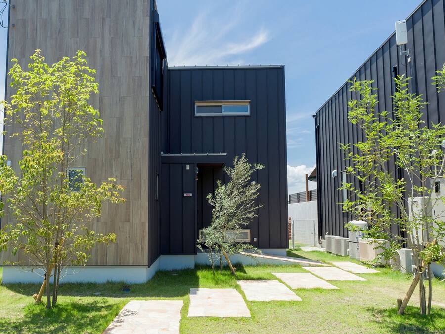Un bâtiment moderne à la façade sombre, avec une clôture en bois et un ciel dégagé.