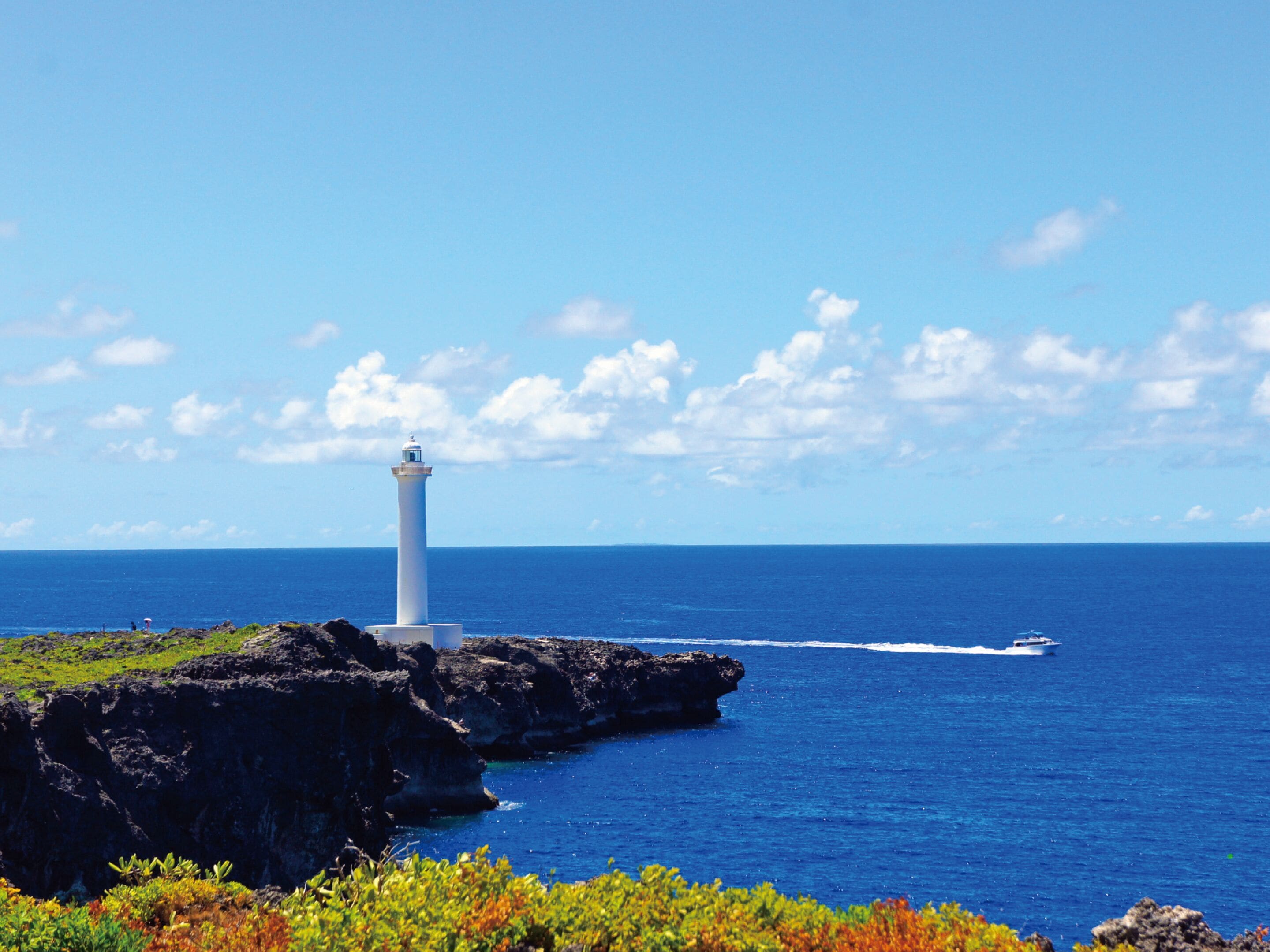 A lighthouse on a rocky outcrop with clear blue skies and calm sea.