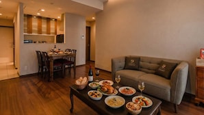 A modern living room with a dining area, wooden flooring, and a sofa with a logo. - THE HOTEL CHATAN by SUNREST RESORT (Chatan)
