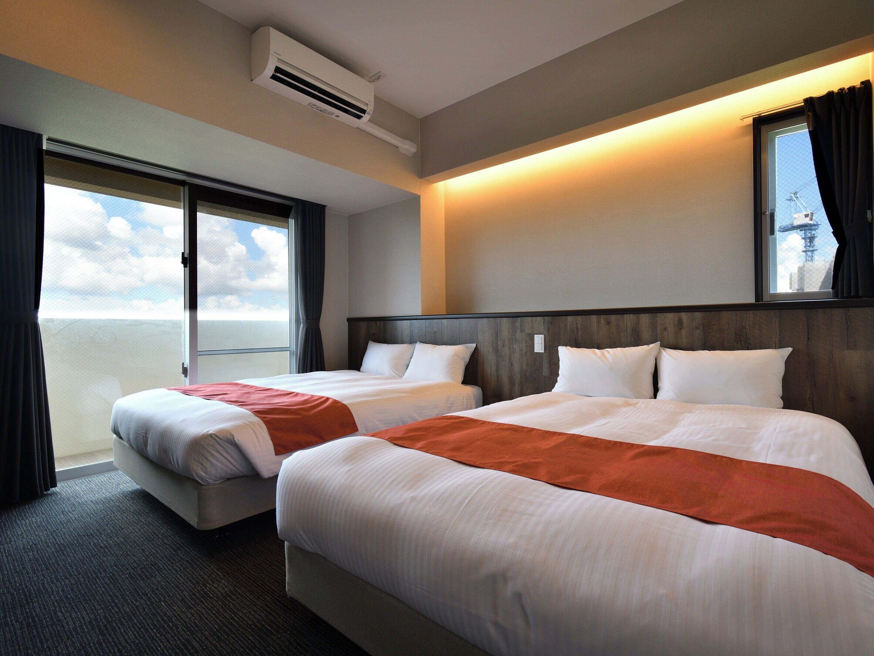 Habitación de hotel con dos camas, un ventanal grande y un equipo de aire acondicionado.