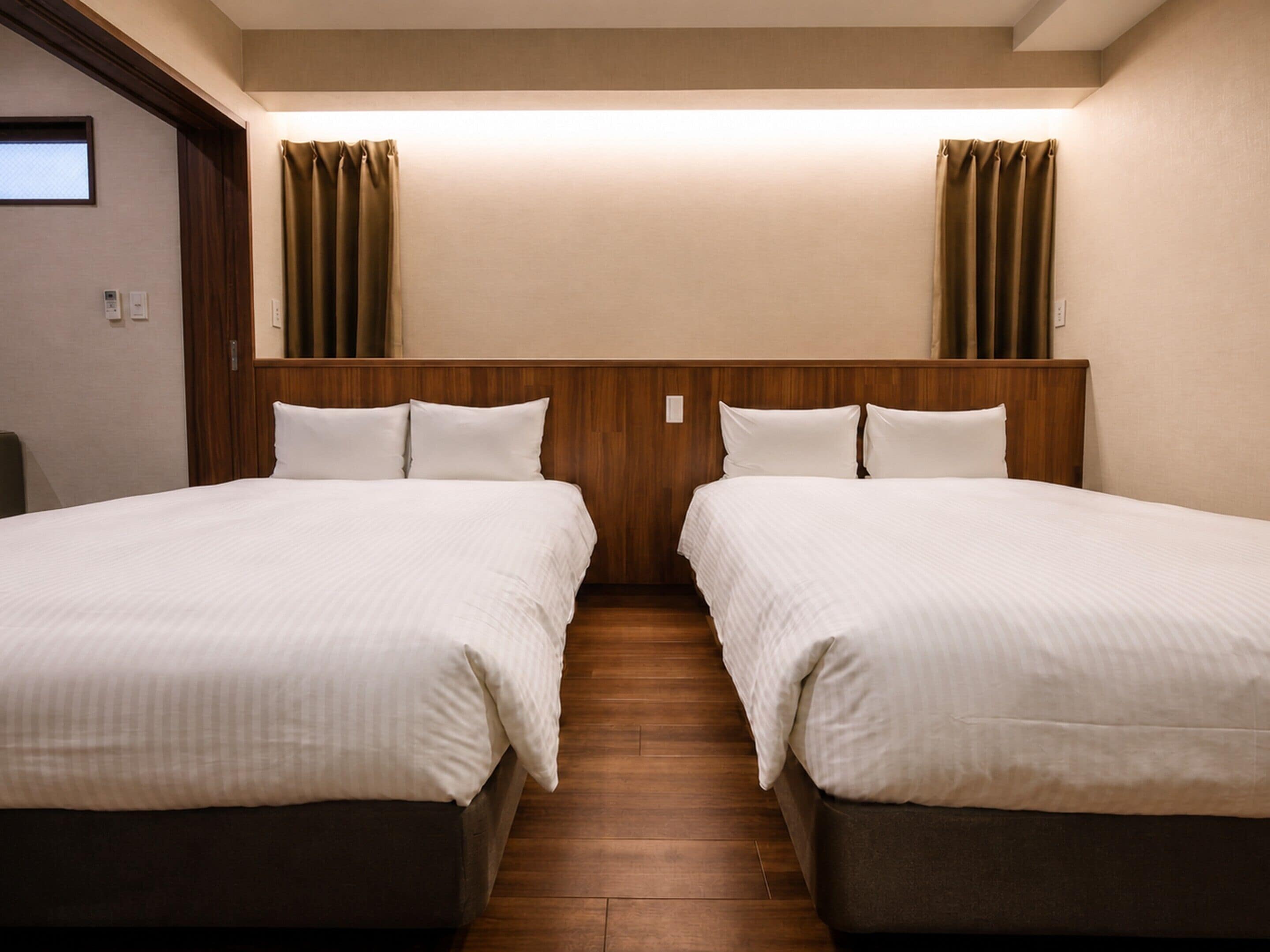 Habitació d'hotel amb dos llits, un capçal de llit de fusta i un paviment de fusta.