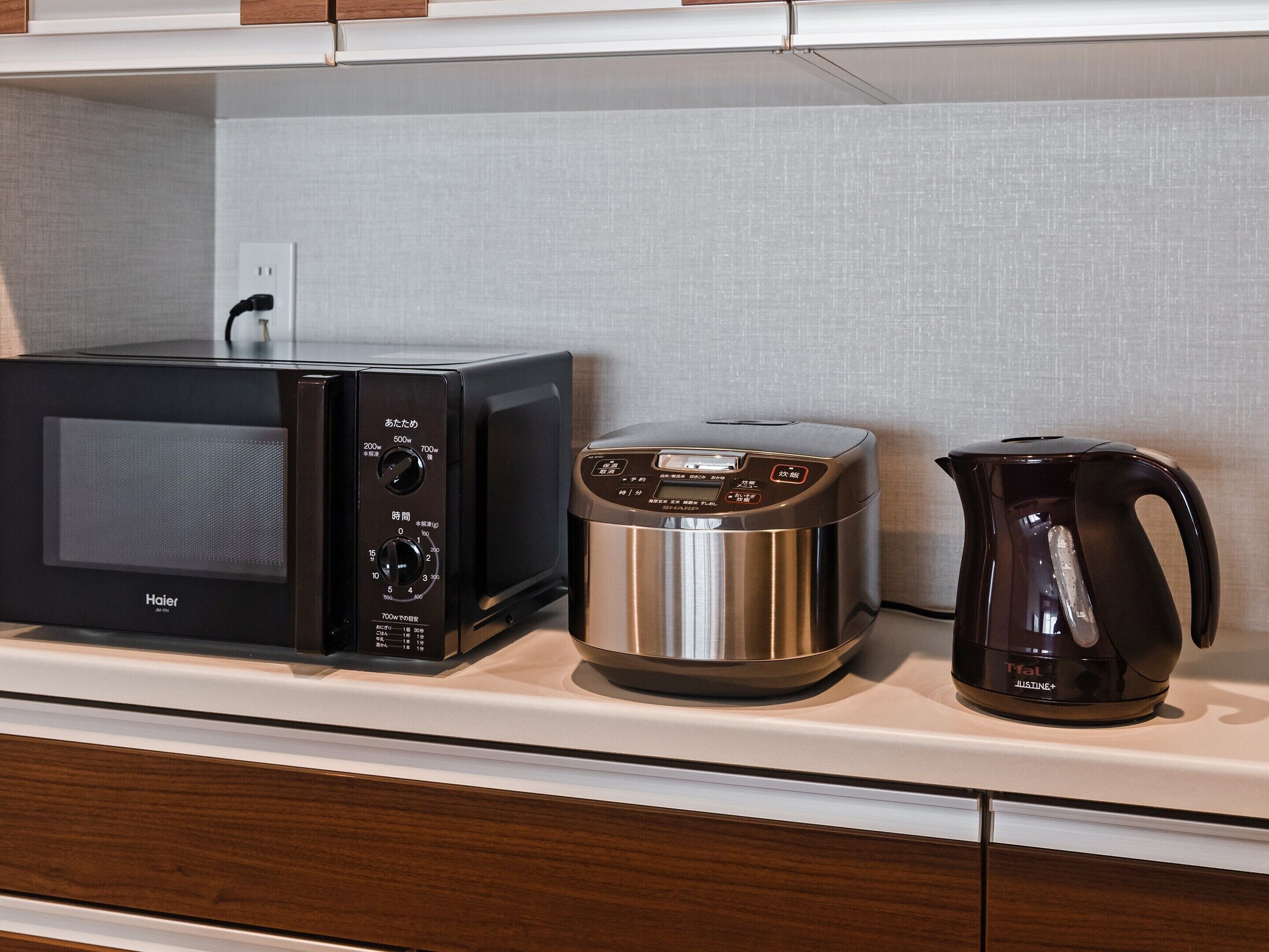 A kitchen with a microwave, a rice cooker, and a coffee maker on the countertop.