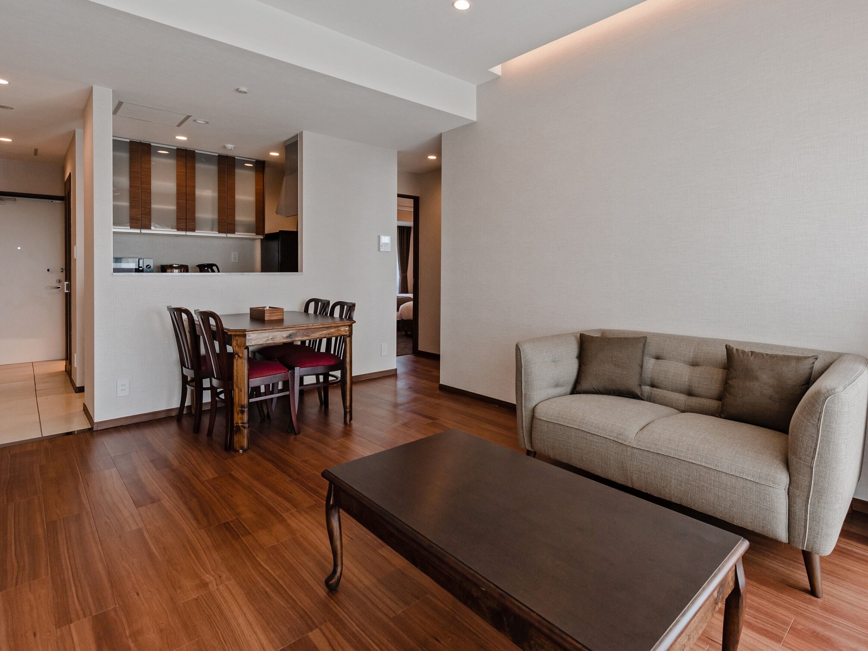 A modern living room with a sofa, a dining table with chairs, and a kitchen area visible through an open door.