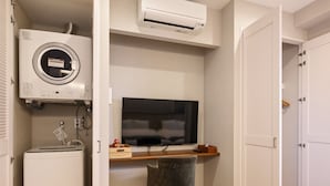A compact room with a bed, a desk with a chair, a television, and a washing machine. - THE HOTEL CHATAN by SUNREST RESORT (Chatan)