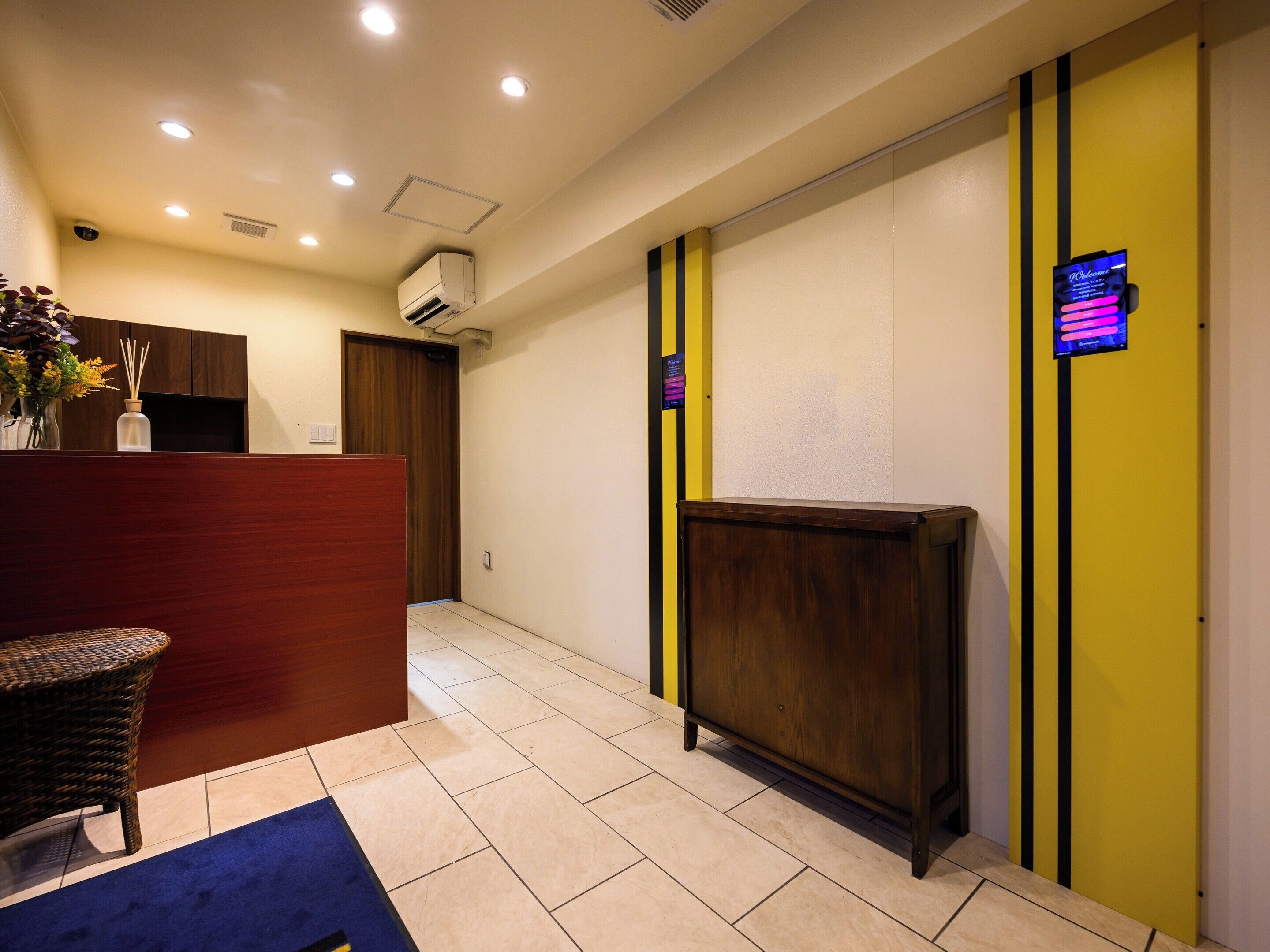 A reception area with a wooden reception desk, a wicker chair, a blue carpet, and a digital welcome screen.