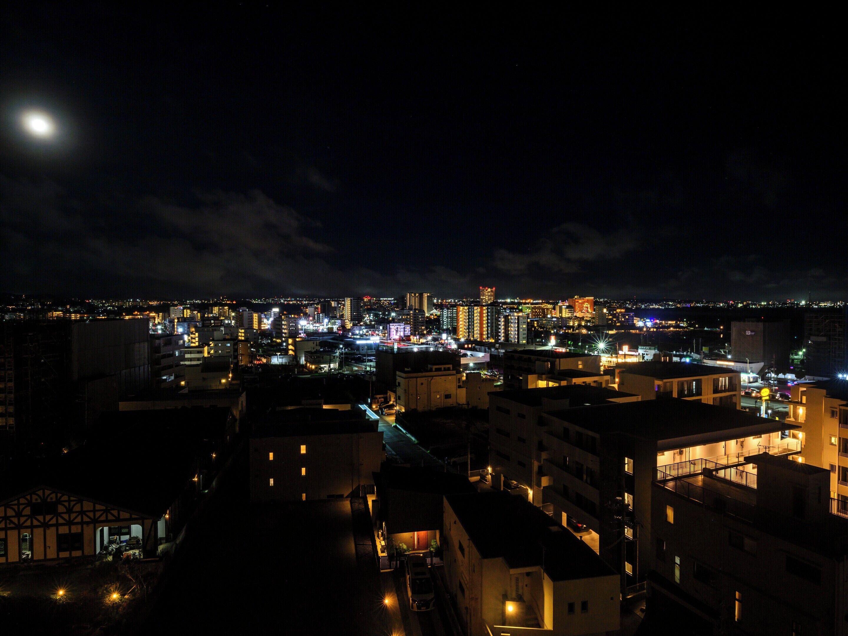 A nighttime cityscape with illuminated buildings and a visible moon.