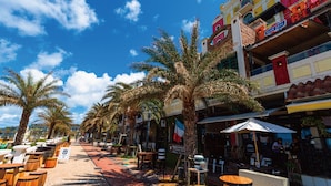 A sunny street lined with palm trees and outdoor seating, with a colorful building featuring a blue sign. - THE HOTEL CHATAN by SUNREST RESORT (Chatan)