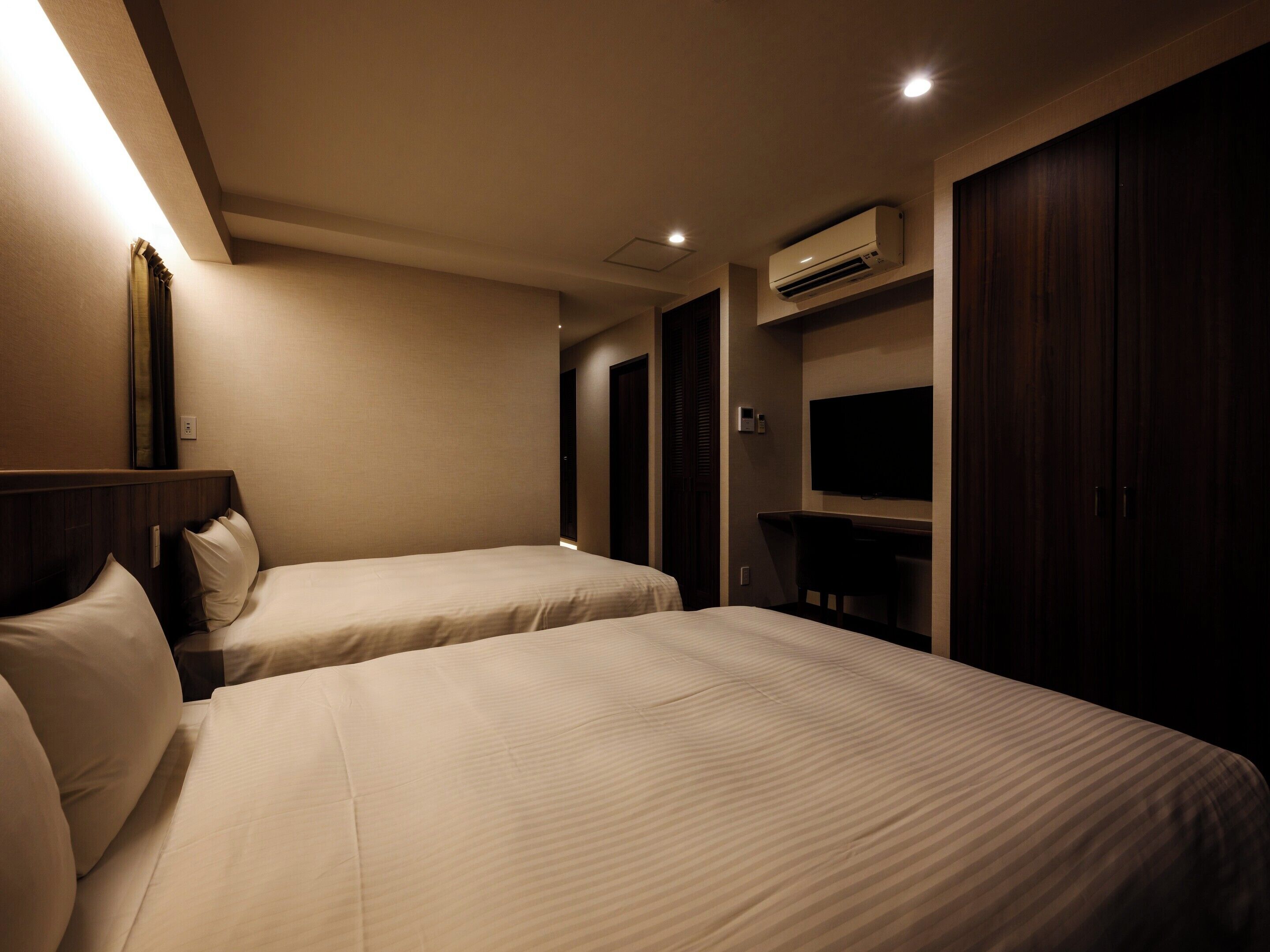 A hotel room with two beds, a TV, and an air conditioning unit.
