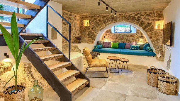 Un intérieur chaleureux avec un mur en pierre, un escalier en bois, un canapé bleu et un téléviseur fixé au mur.