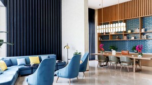 Una sala moderna con un sofá modular, sillones azules, una mesa de comedor con sillas, una estantería y un candelabro decorativo.