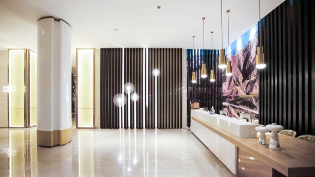 Un moderno vestíbulo de hotel con un mostrador de recepción, un televisor grande montado en la pared y luminarias contemporáneas.