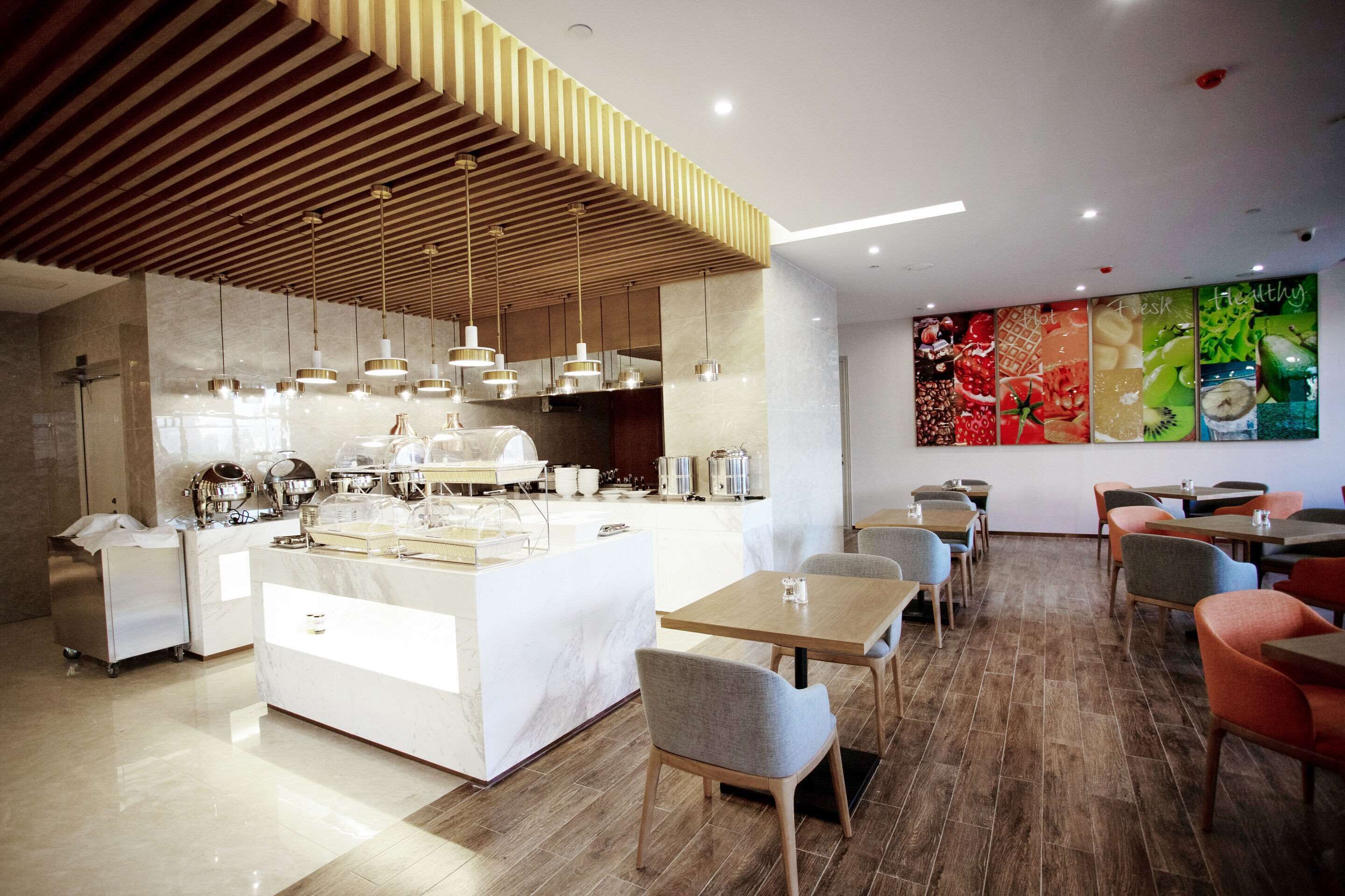 Ein modernes Restaurant mit einer zentralen Kochinsel, Holzbalkendecke und einer farbenfrohen Wand mit Lebensmittelauslagen.
