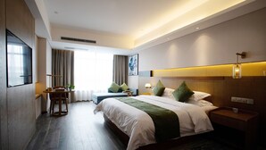 Una habitación de hotel moderna con una cama grande, un escritorio y una silla. Hay una ventana con cortinas, un televisor montado en la pared y una mesita de noche con una lámpara.