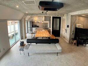 A modern kitchen with a wooden table and bench, a piano, and a large window. - Guest House Matsu Bekkan (Osaka)