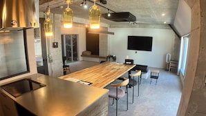 A modern kitchen with a large island, pendant lighting, a flat-screen TV, and a view of the outdoors. - Guest House Matsu Bekkan (Osaka)