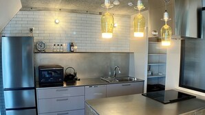 A modern kitchen with stainless steel appliances, a wooden island, pendant lights, and a brick backsplash. - Guest House Matsu Bekkan (Osaka)