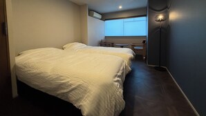 A hotel room with two beds, a desk, a chair, a lamp, and a window with blinds. - Guest House Matsu Bekkan (Osaka)