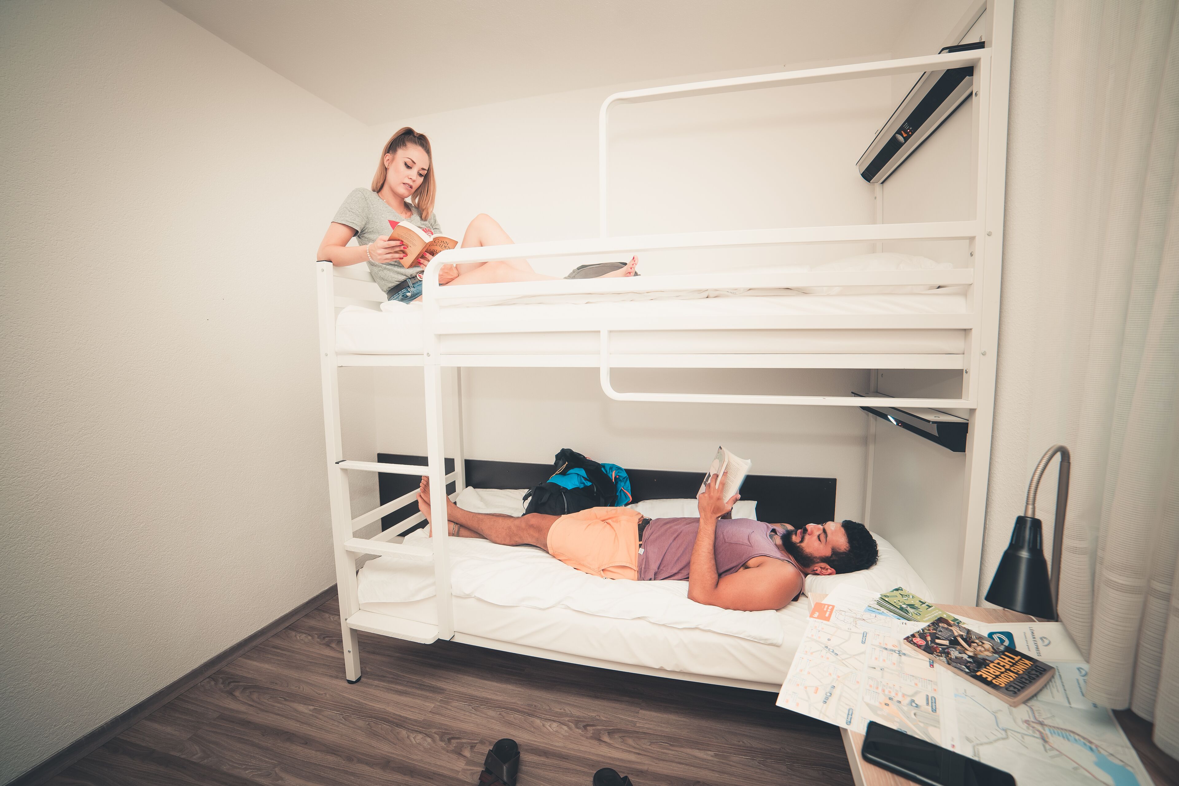 Une chambre avec un lit superposé, où une personne est assise en haut et lit, et une autre personne est allongée en bas.