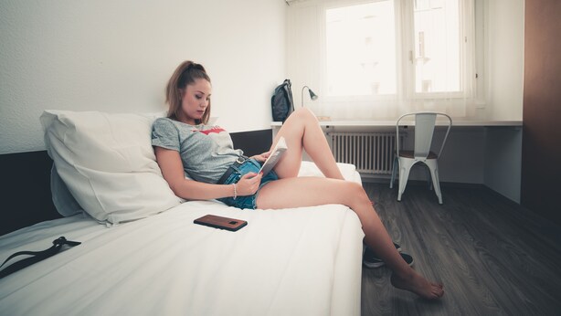 Une personne allongée sur un lit dans une pièce qui contient une fenêtre, un radiateur et une chaise.