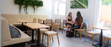 Un café moderno con mesas y sillas de madera, un sofá y una pared cubierta de plantas verdes.