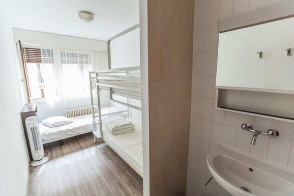 A room with bunk beds, a white radiator, a white sink, and a window with blinds.