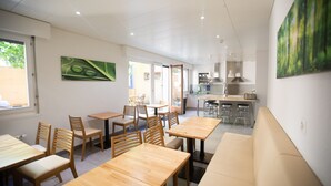 Un espace repas moderne avec des tables et des chaises en bois, un banc et une cuisine en arrière-plan.