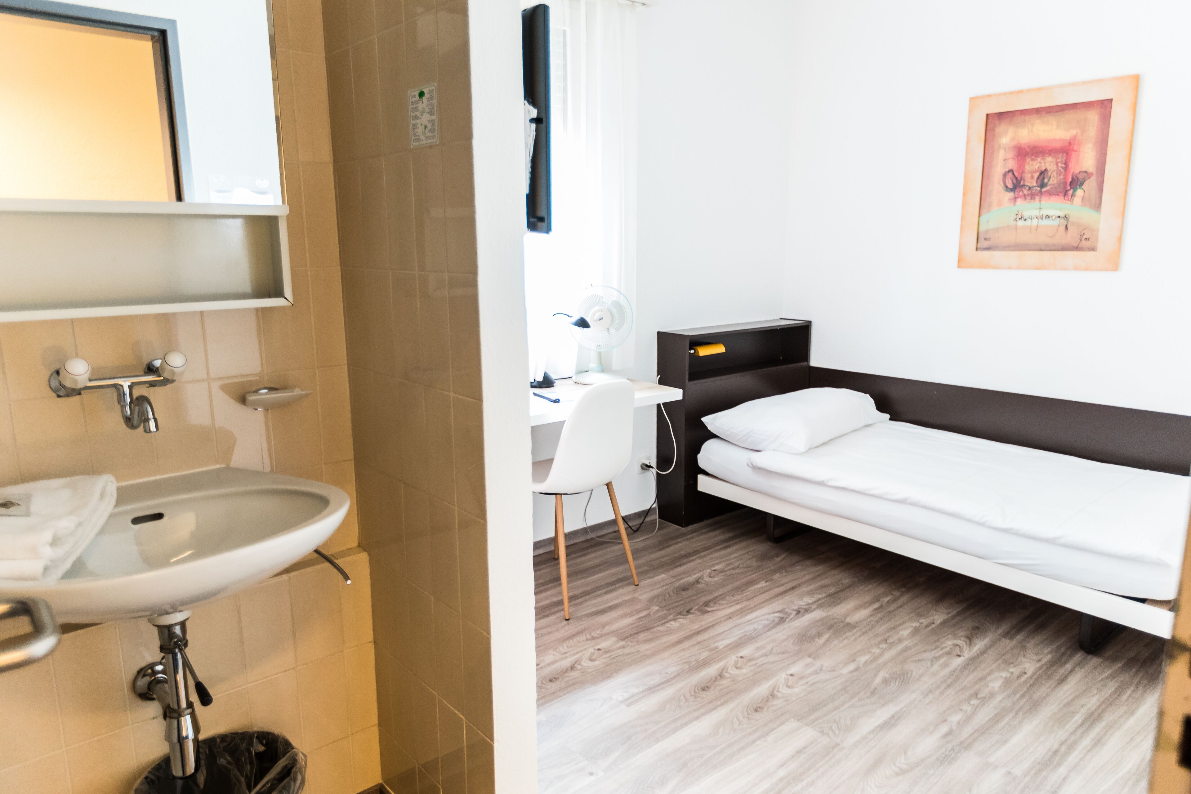 A hotel room with a white sink, a bed, a desk, and a chair.