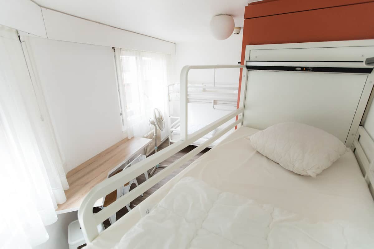 A hospital room with a bed, white curtains, a window, and a radiator.
