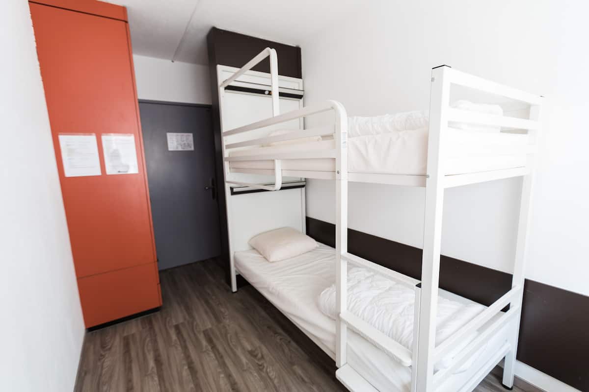 A bunk bed room with a wooden floor, a red cabinet, and a door with a notice.