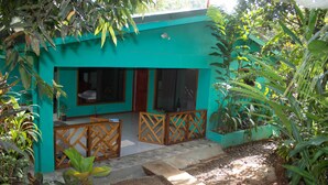 A turquoise building with a balcony, potted plants, and a tiled floor.