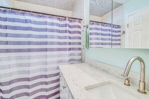 Un baño con cortina de ducha a rayas, un lavabo de mármol y un espejo encima.