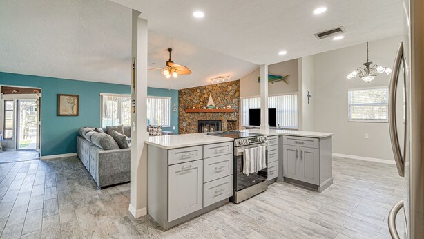 A spacious kitchen with a stone fireplace, a large island with a stove, and a ceiling fan. - Private Dock: Riverfront Homosassa Home! (Homosassa)