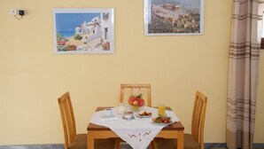 A dining table with a white tablecloth, two wooden chairs, and a breakfast setting including a plate of fruit, a glass of juice, and a cup of coffee. - Moustakis Hotel (Kefalonia)