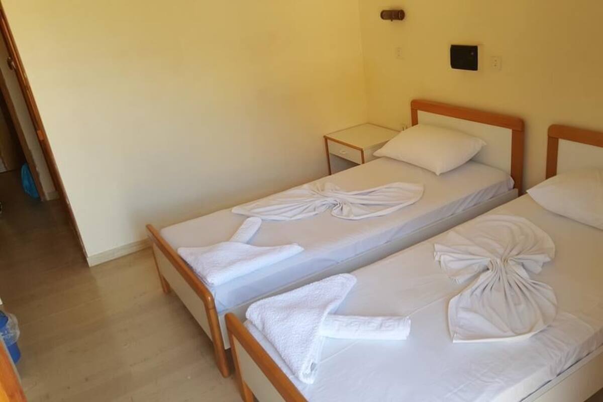 Hotellihuone, jossa on kaksi erillistä sänkyä, ja kummankin sängyn päällä on siististi taitettu pyyhe sekä pieni yöpöytä.