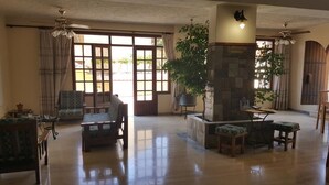 A spacious living area with a stone fireplace, comfortable seating, and large windows allowing natural light. - Moustakis Hotel (Kefalonia)