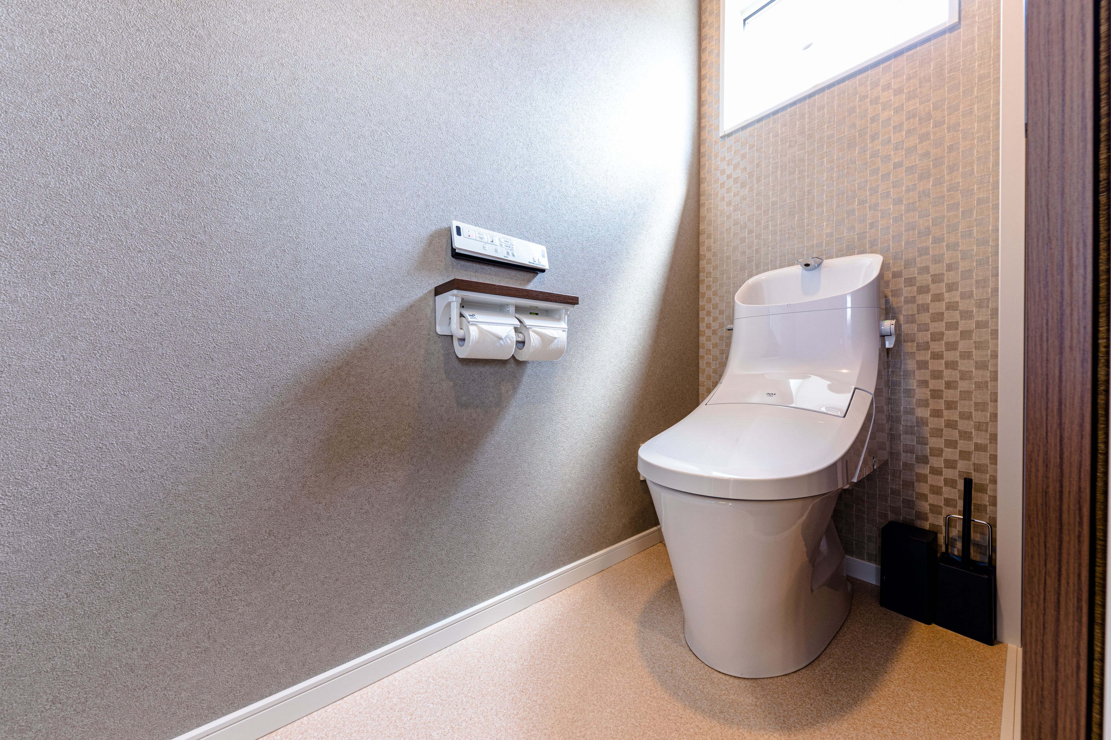 A modern bathroom with a toilet, a wall-mounted toilet paper holder, and a small trash bin.