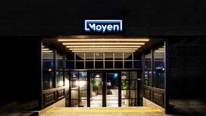 A modern building entrance with a 'Moyen' sign, glass doors, and a yellow tactile paving strip. - Moyen Hotel (Sokcho)