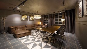 A modern room with a brown leather sectional sofa, a wooden dining table with chairs, a patterned floor, and framed artwork on the walls. - Moyen Hotel (Sokcho)