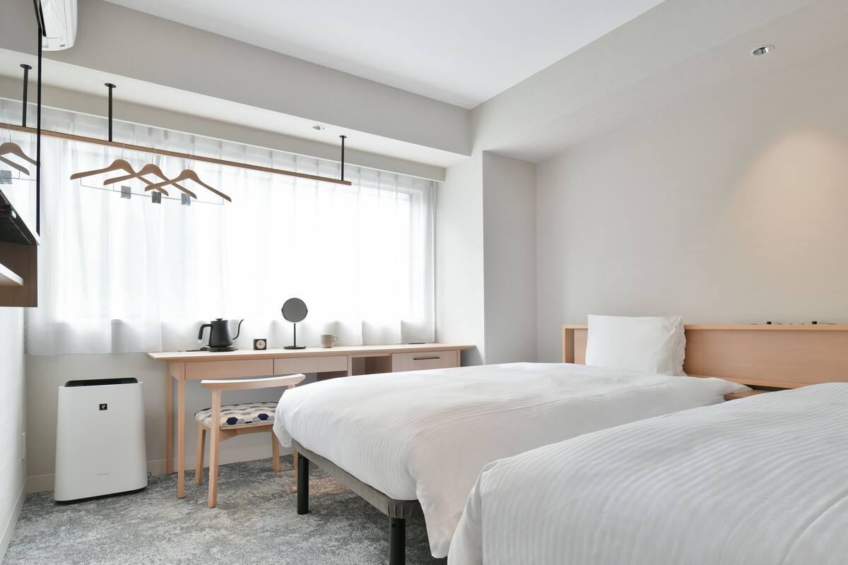Una habitación de hotel moderna con una cama grande, un escritorio con una silla, un radiador pequeño y una ventana con cortinas.