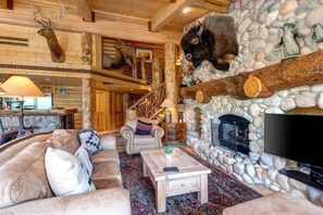 A log cabin interior with a stone fireplace, mounted animal heads, a television, and a cozy seating area.