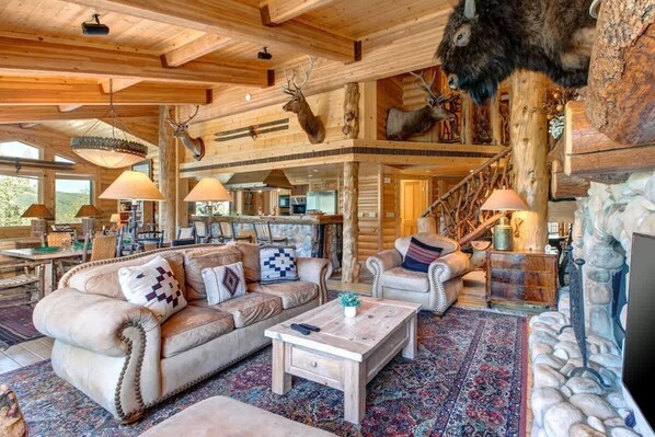 A log cabin interior with a fireplace, leather sofas, and antler decorations.