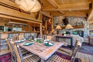 A rustic wooden interior with a dining table set for four, a stone fireplace, and a cozy seating area.