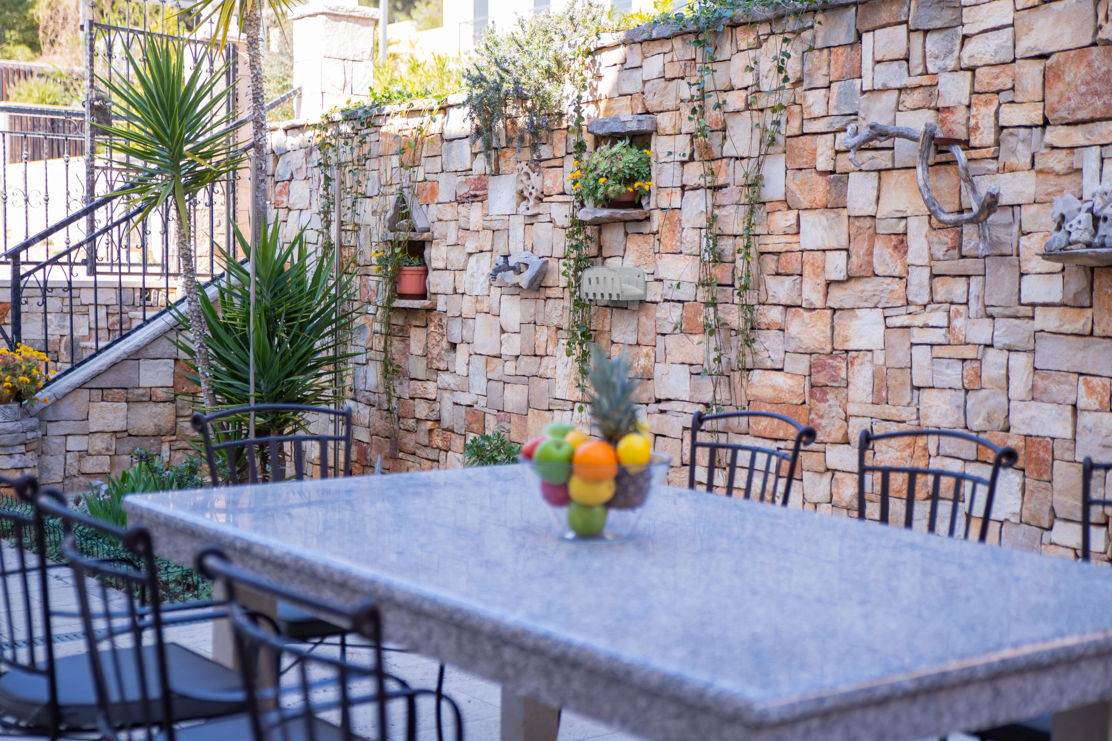 A stone wall with plants and a fruit bowl on a table.