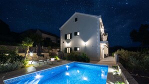 Una piscina con vista sul cielo notturno, un edificio bianco con balconi e zone relax all'aperto.