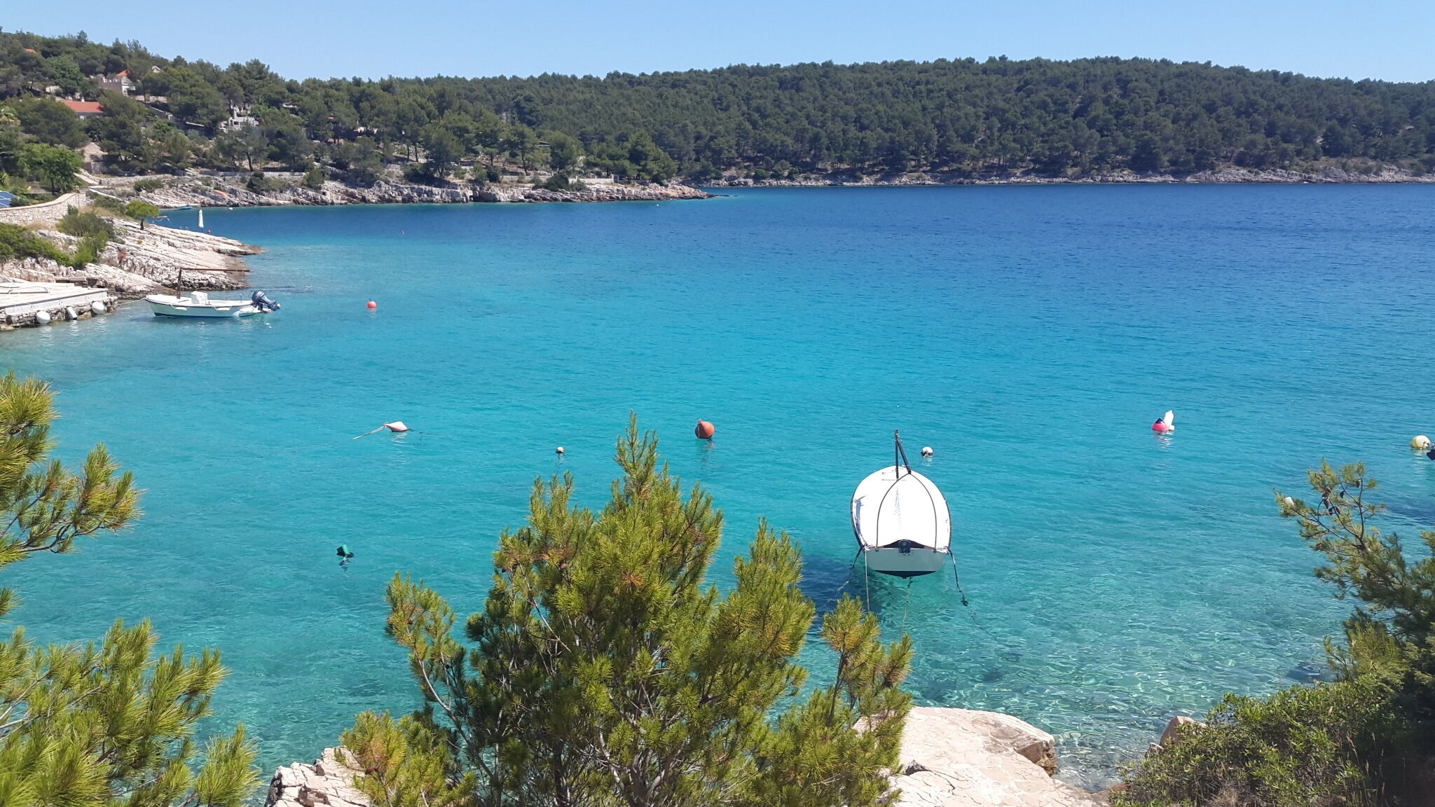 Une zone côtière caractérisée par une eau turquoise et limpide, des bateaux et une côte rocheuse bordée d’arbres.