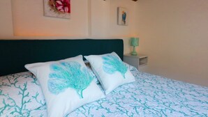 A bedroom with a bed, two pillows with tree designs, a nightstand with a lamp, and a wall with a flower painting and a small portrait.