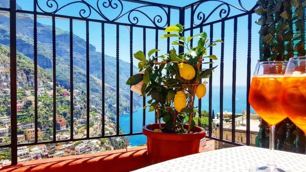 A balcony with a potted lemon tree, a table, and a glass of orange beverage. - CASA ALESSANDRA in Positano (Positano)
