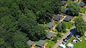 An aerial view of a residential area with multiple houses, a parking lot, and a dense forest surrounding the properties. - Bungalows an der Ostsee (Kołobrzeg)